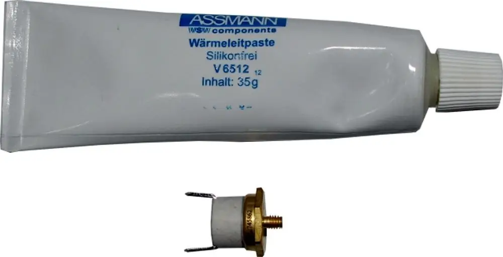 Weißer Tuben mit Wärmeleitpaste und einem Metallteil, das möglicherweise eine Verbindungskomponente ist, vor neutralem Hintergrund. Herstellerinfo nicht sichtbar, aber relevant für Wolf-Produkte.